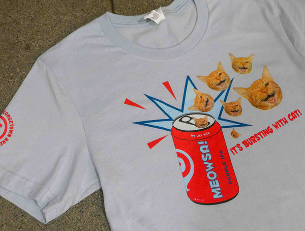 a light blue shirt with a cartoon style red meowsa can and multiple cat heads coming out of the opening of the can. text reads "it's bursting with cat!"